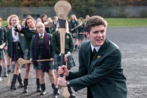 still from Derry Girls with Dylan Llewellyn holding a hurl